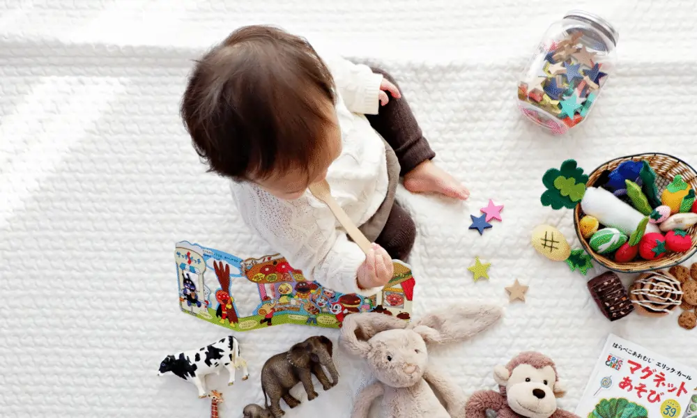 Baby on white carpet with toys and spoon