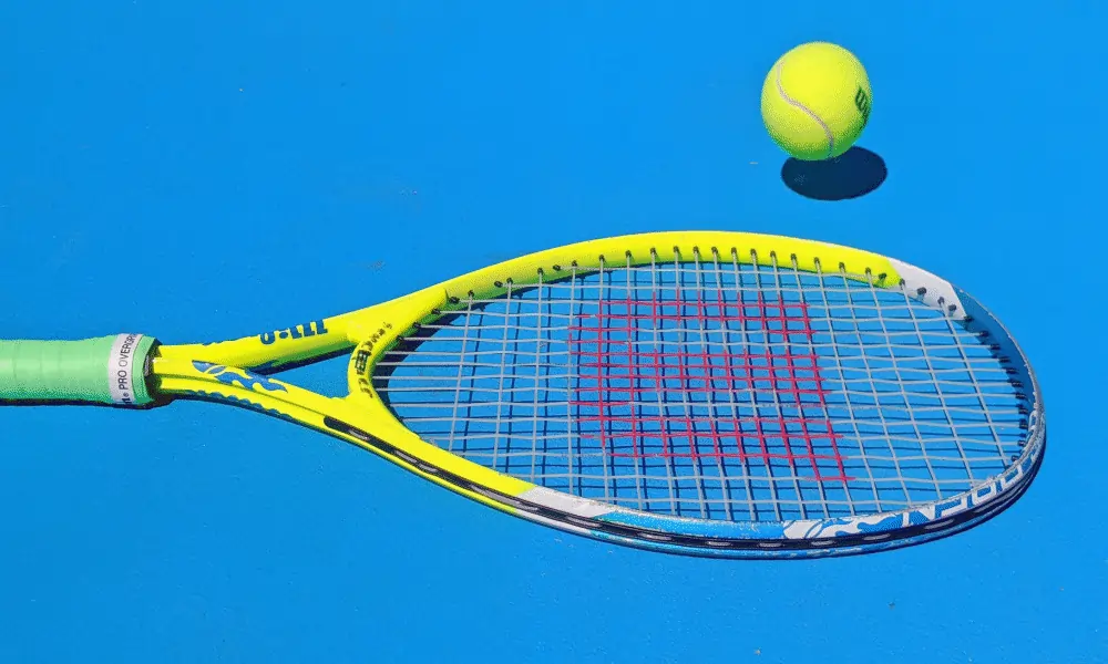 Bild von Tennisschlaeger von Wilson in gelb auf blauem Tennisplatz mit gelben Tennisball