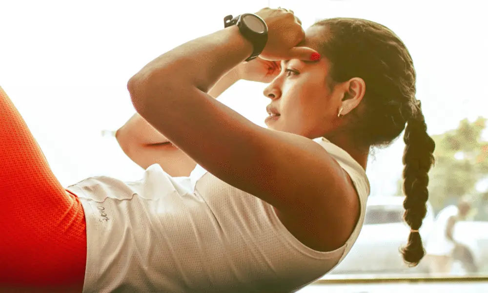 Bild von Frau mit Pferdeschwanz und Fitnesstracker auf linkem Arm auf Yogamatte macht Crunches