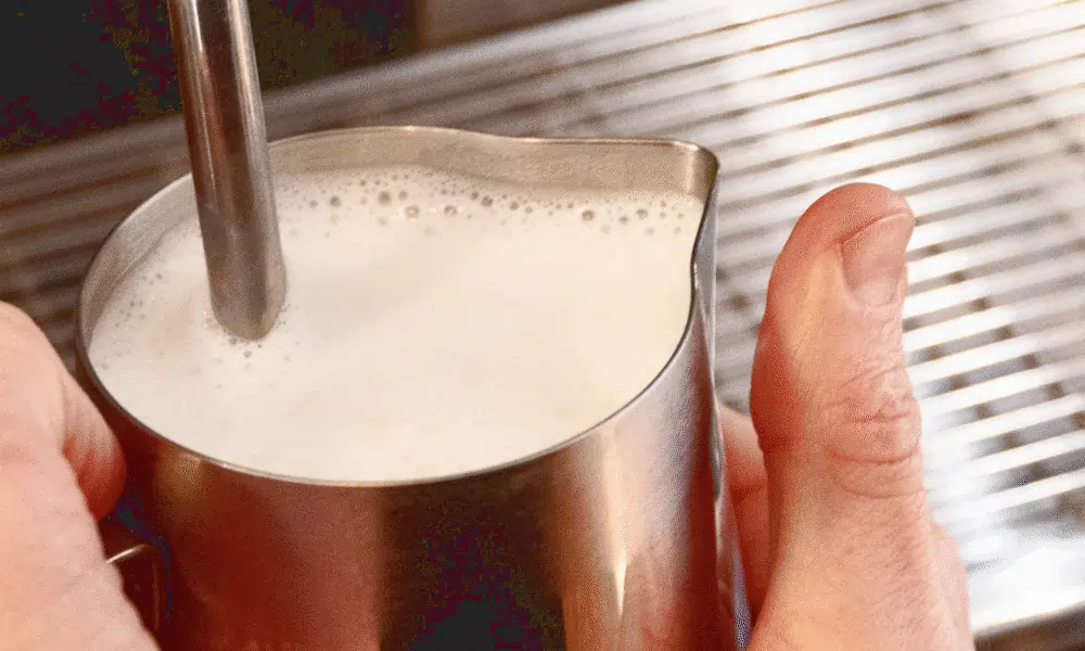 Milch geschäumt in Metallbecher und Daumen von Mann