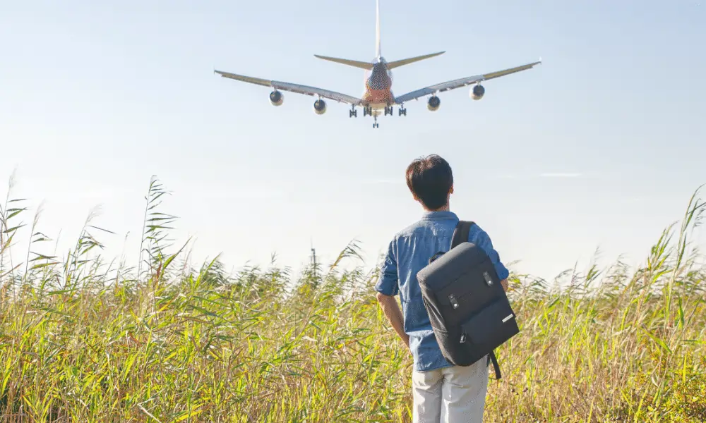 Bild von Mann mit Rucksack am Ruecken und Hintergrund blauer Himmel und Flugzeug